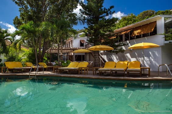 The iconic smile-shaped swimming pool at Gyp Sea Hotel St. Barth, surrounded by lush tropical gardens, cacti, and bright yellow parasols.