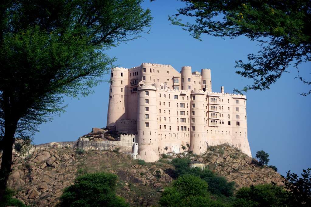 A dramatic dusk view of Alila Fort Bishangarh illuminated atop a granite hill, with the Nazaara terrace visible.