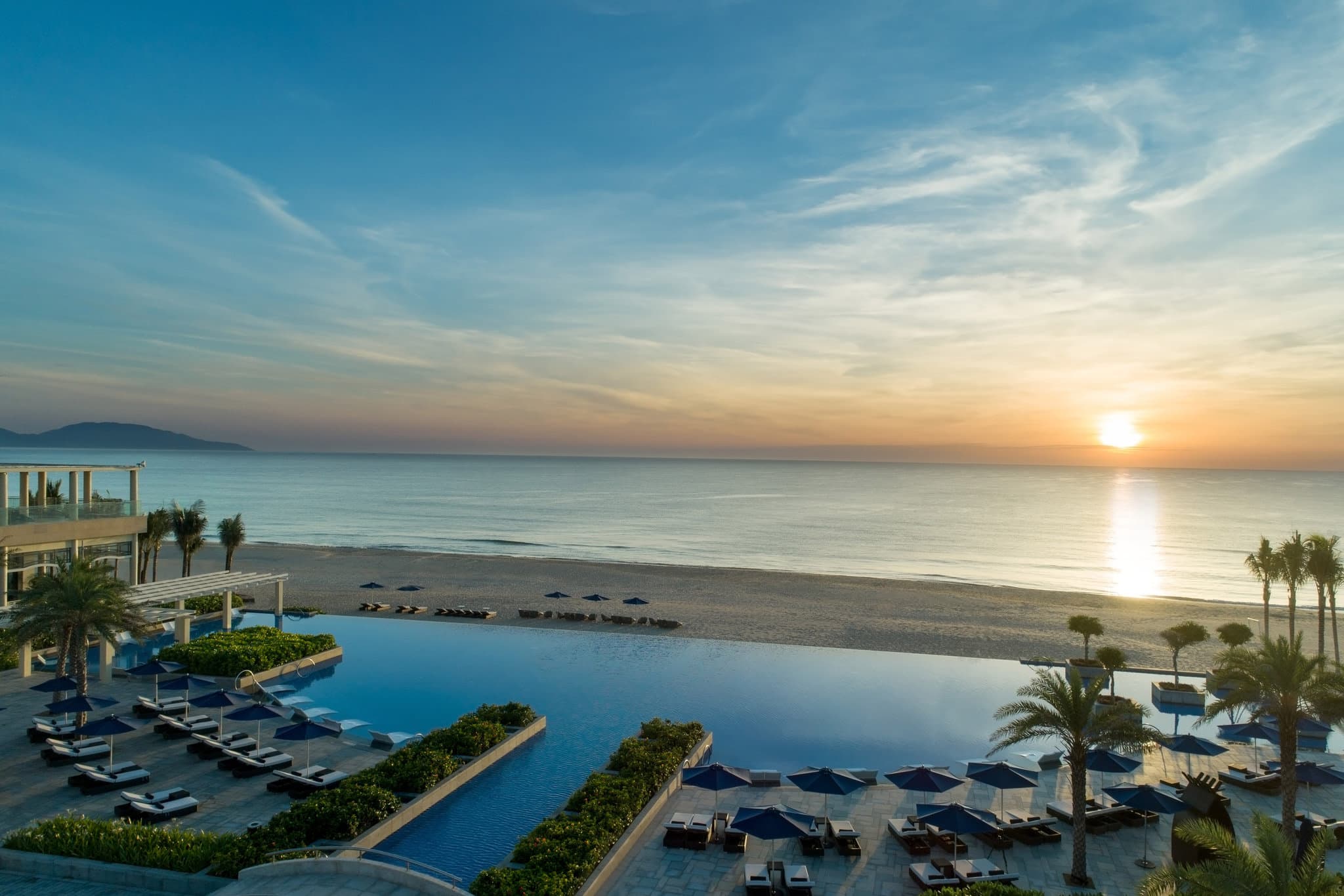 Sheraton Grand Danang 250m infinity pool stretching towards the ocean at sunset with resort facade in background.