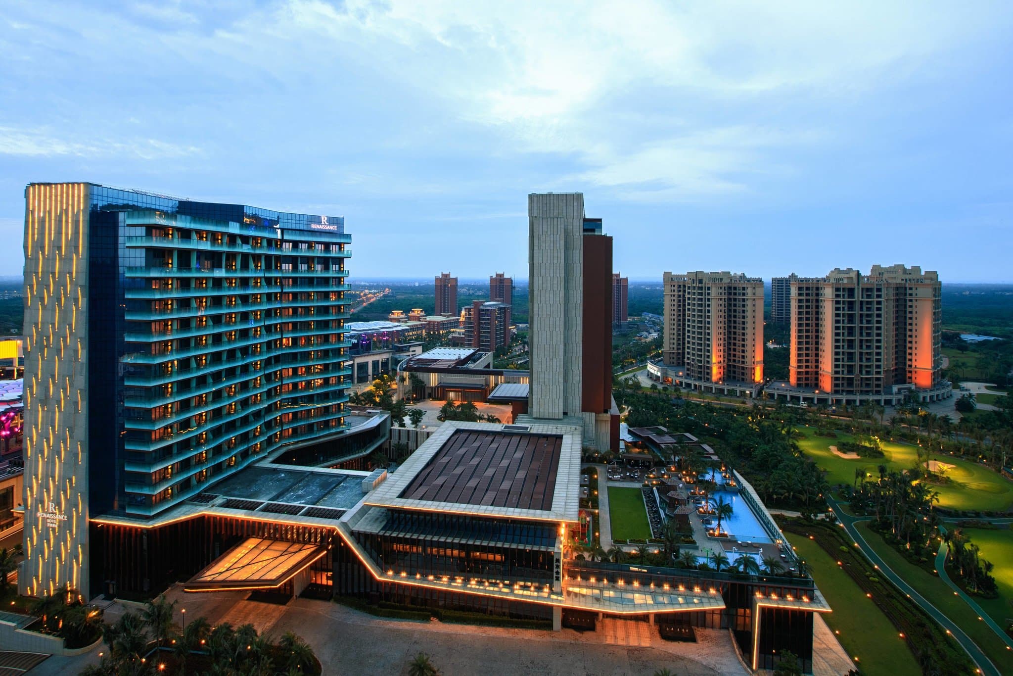 View from Renaissance Haikou balcony overlooking the Mission Hills golf course and outdoor swimming pools at sunset.