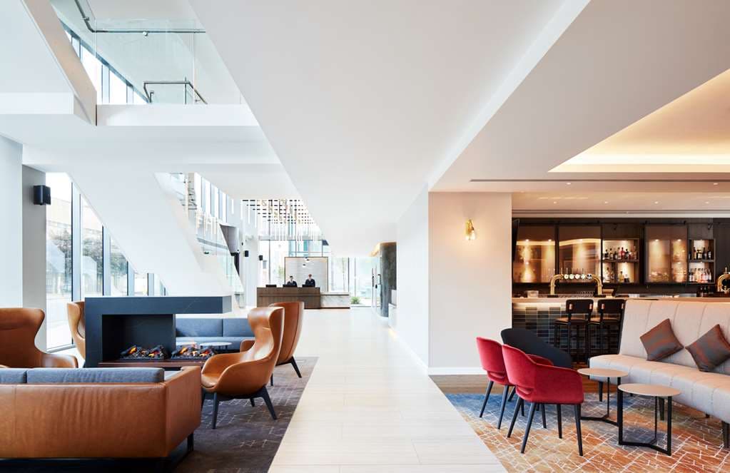A sleek corner hotel room at Hyatt Regency Manchester featuring floor-to-ceiling windows with panoramic city views and modern minimalist furniture.