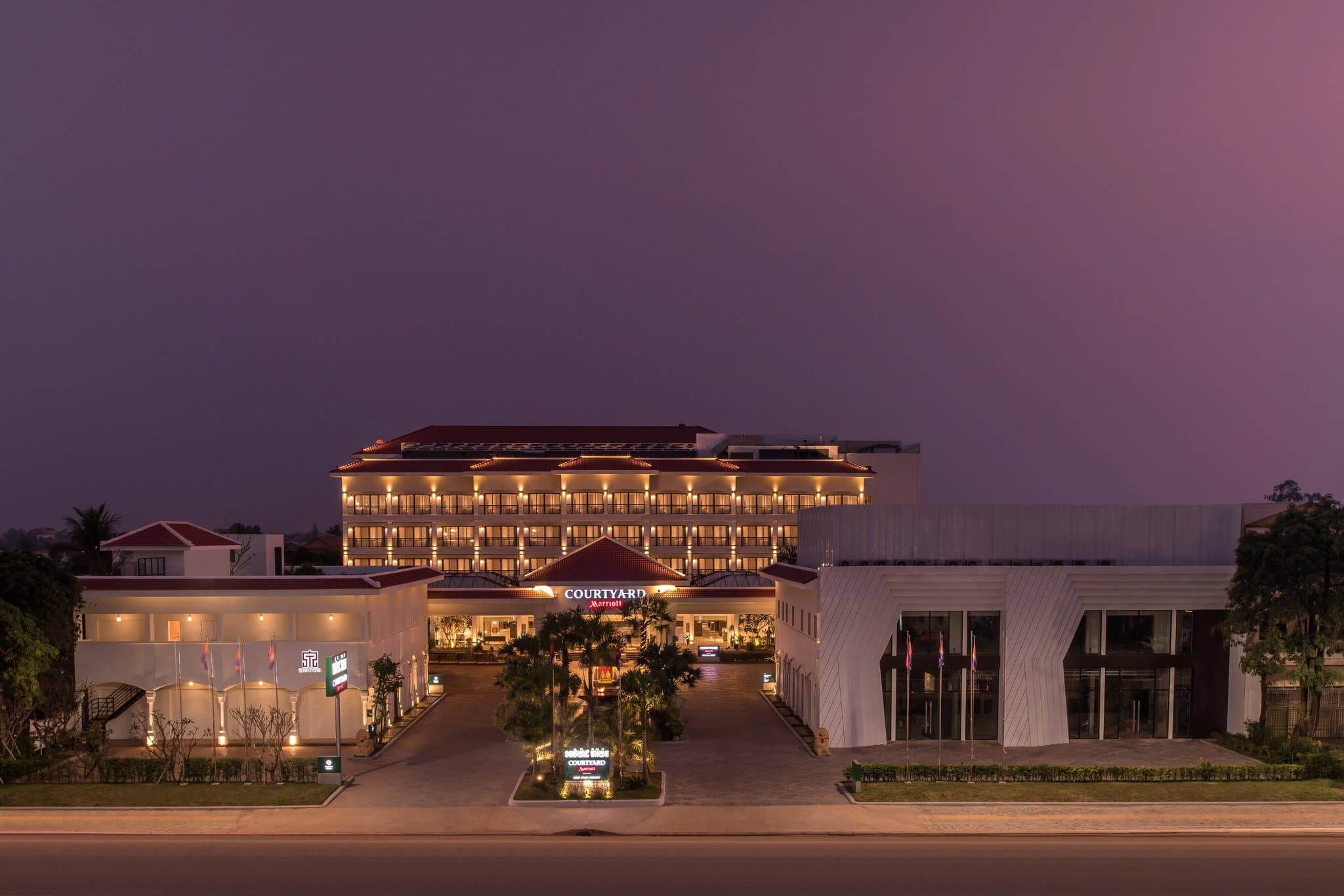 A sprawling saltwater lagoon pool at twilight, flanked by modern Khmer architecture and illuminated by warm, ambient lighting.