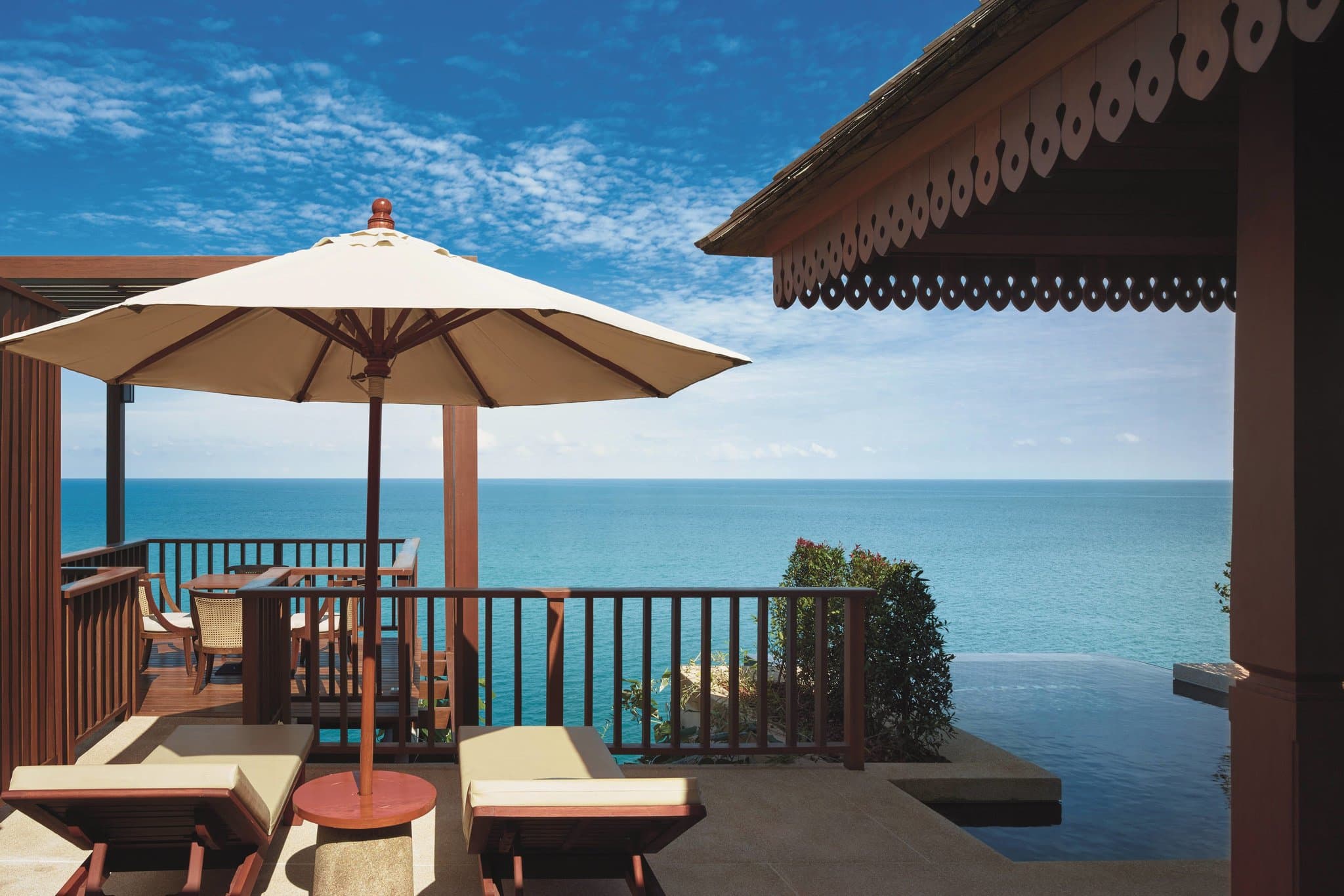 Aerial view of The Ritz-Carlton Koh Samui showcasing terraced white villas cascading down a lush green hillside toward a circular saltwater Swim Reef and the ocean.