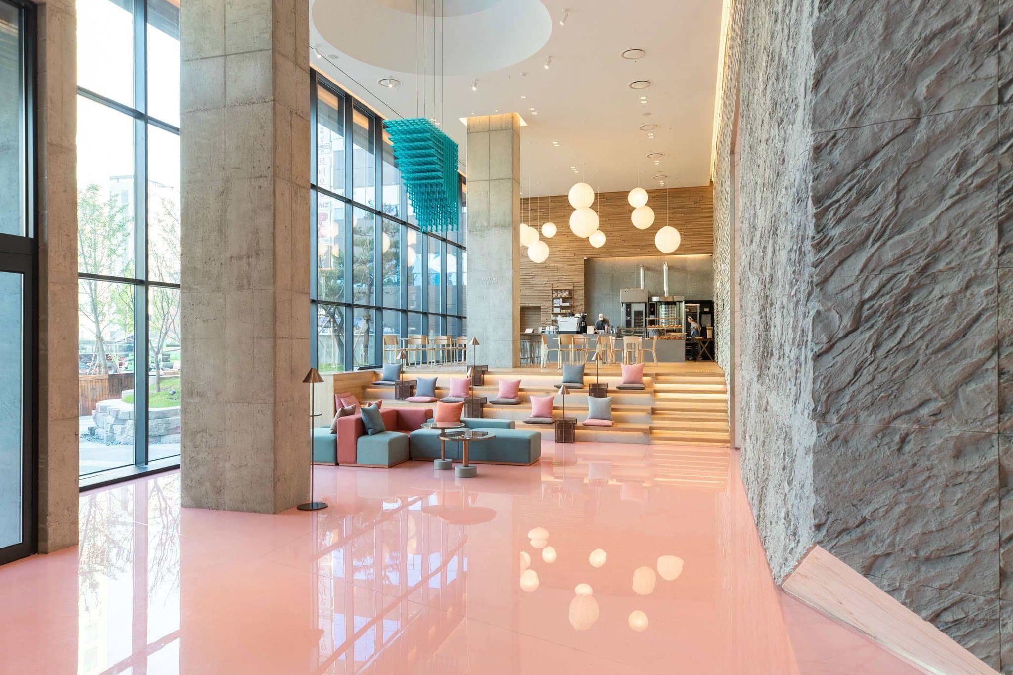 Lobby of RYSE hotel in Seoul featuring glossy pink resin floors, concrete stadium-style seating, and modern art installations.