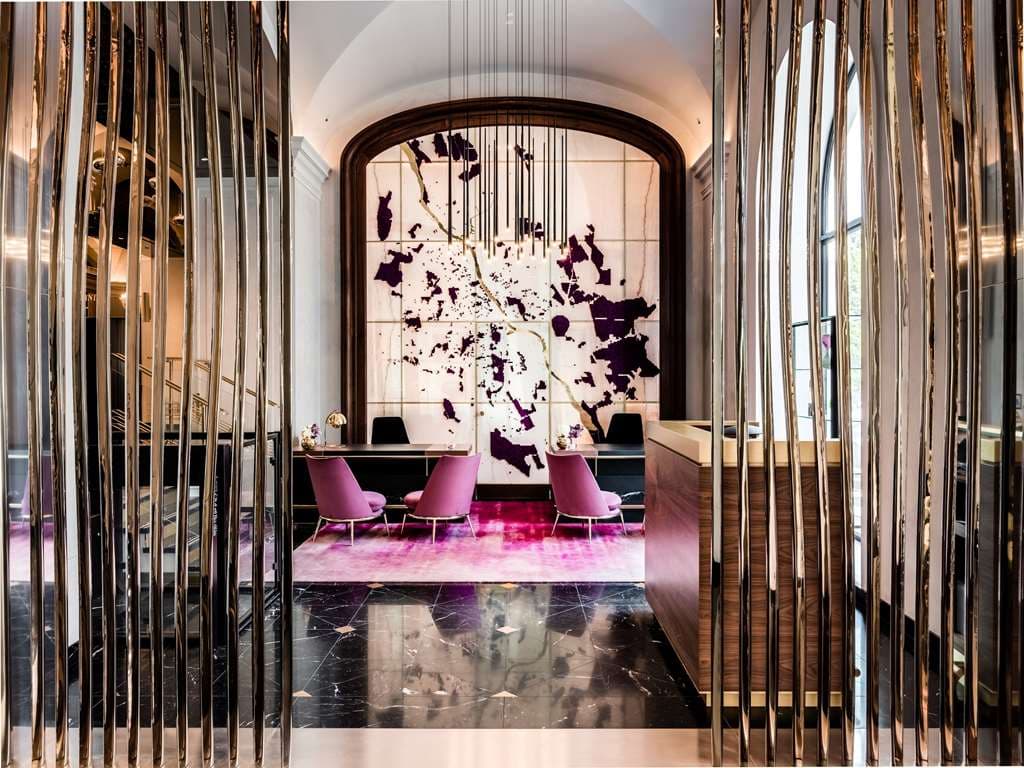 The long, sleek marble counter of the Long Bar at Raffles Europejski Warsaw, illuminated by warm amber lighting with plush velvet bar stools.