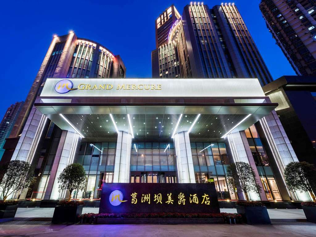 A moody, blue-toned indoor swimming pool at Grand Mercure Wuhan Qiaokou with floor-to-ceiling windows.