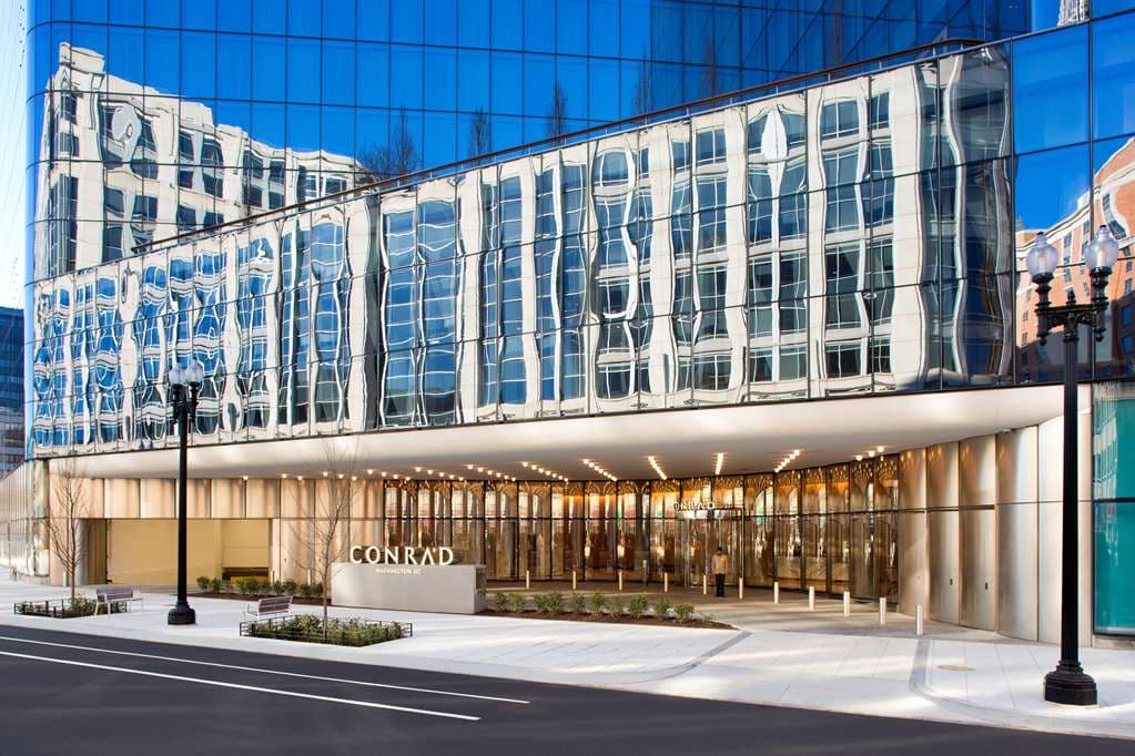 The soaring, light-filled atrium of Conrad Washington DC featuring the 'Falling Flowers' chain-link art installation above a sleek marble lobby.