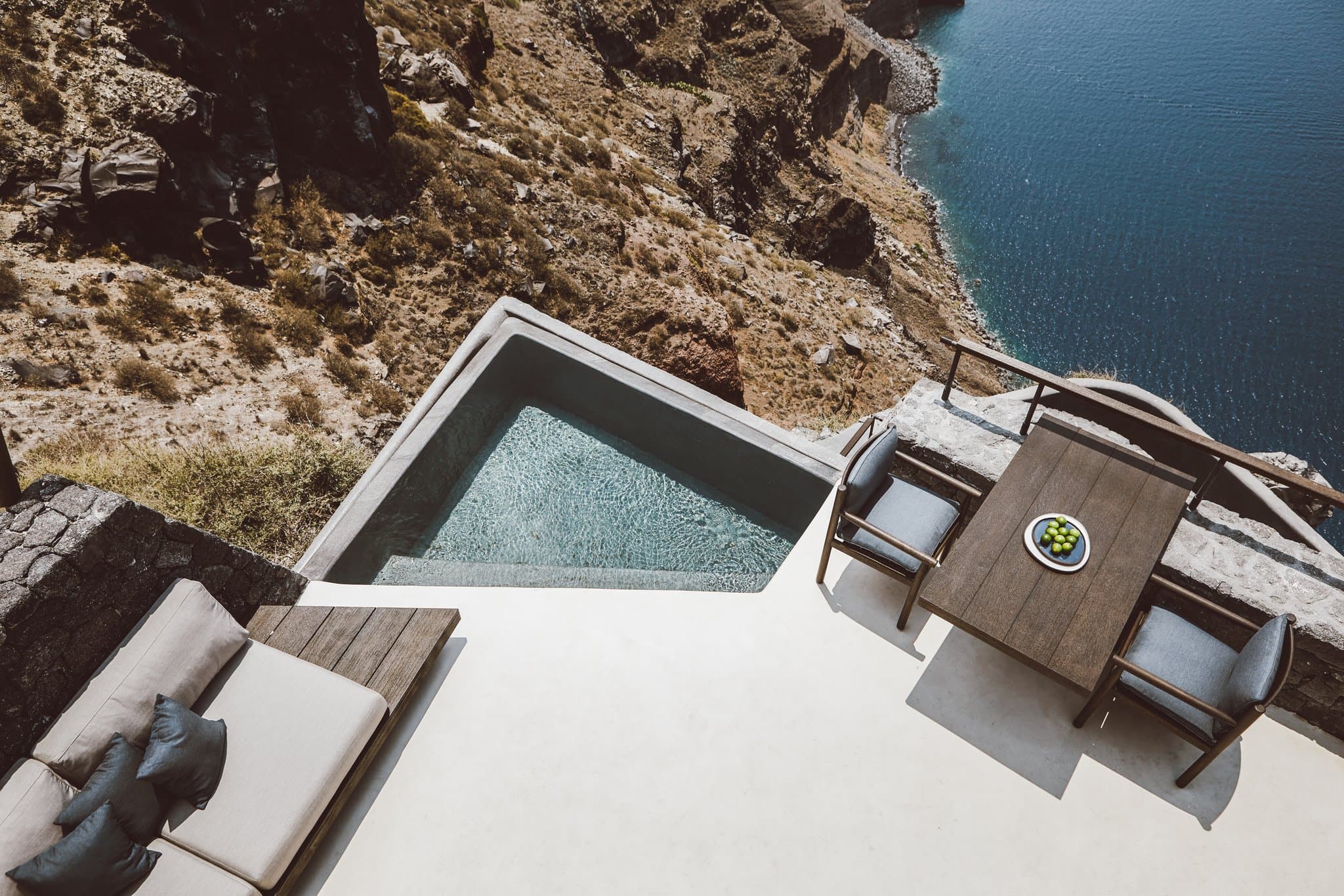 A sharp, zigzagging white staircase cutting dramatically through dark, jagged volcanic rock against the deep blue Aegean Sea at Vora Santorini.