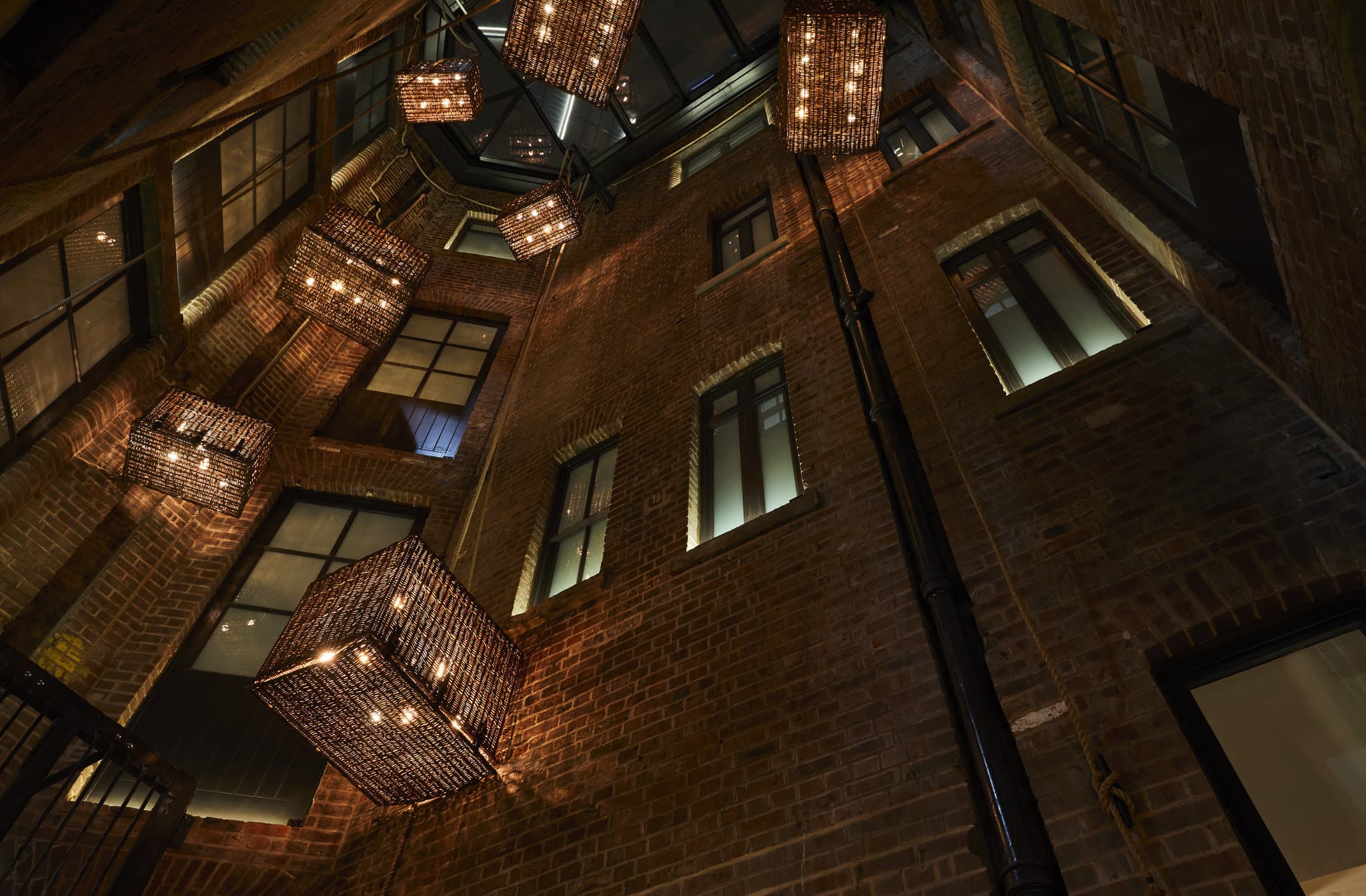 Hotel Indigo Manchester lobby atrium featuring restored red brick arches, industrial pulley lighting, and a modern curved reception desk.