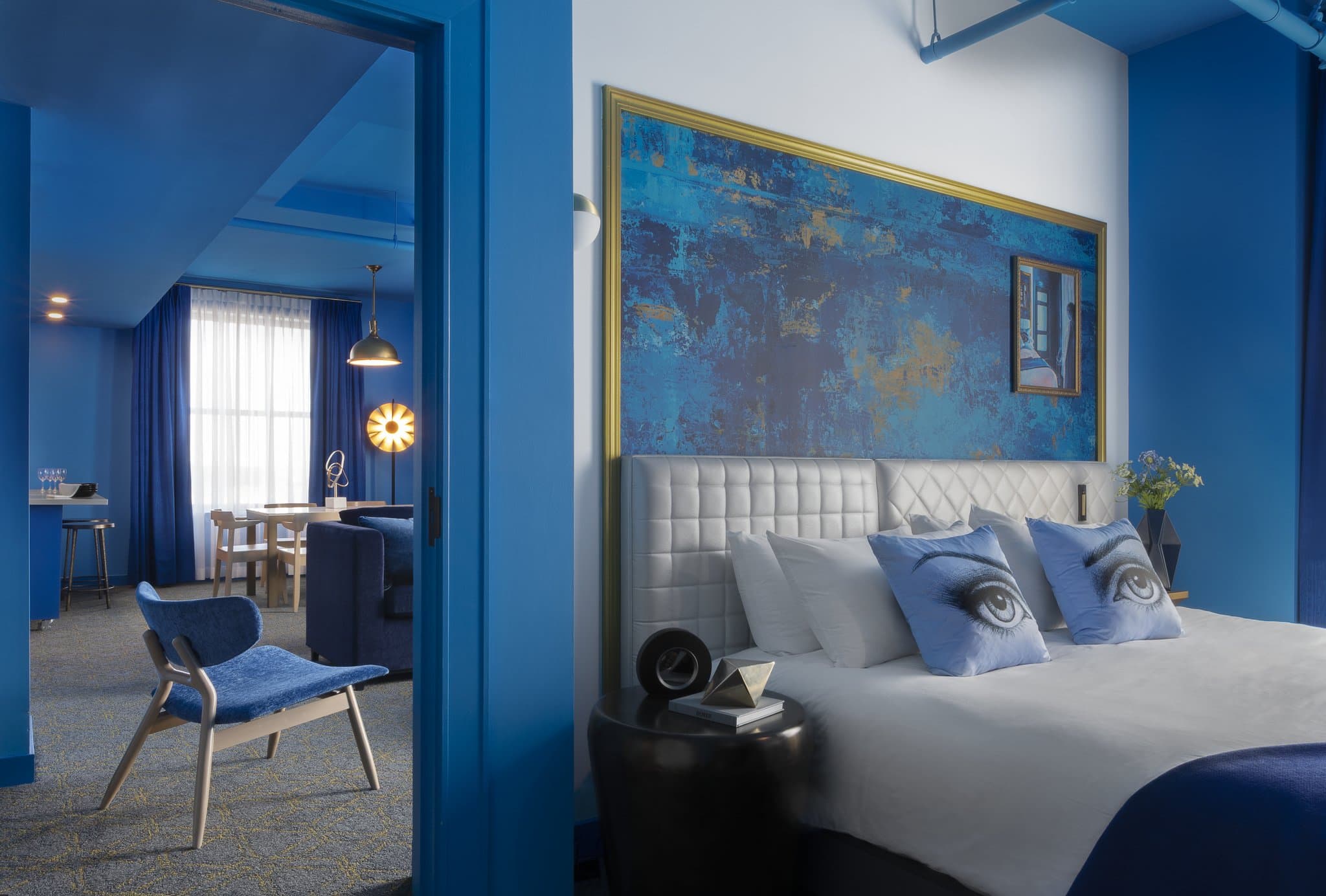 A vibrant, monochromatic blue hotel room at Angad Arts Hotel with a king bed, signature eye pillow, and city views.