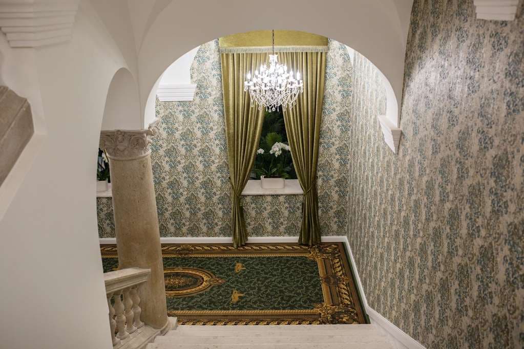 The Great Hall restaurant at Mystery Hotel Budapest featuring a massive crystal chandelier, twin spiral staircases, and Masonic-inspired velvet decor.