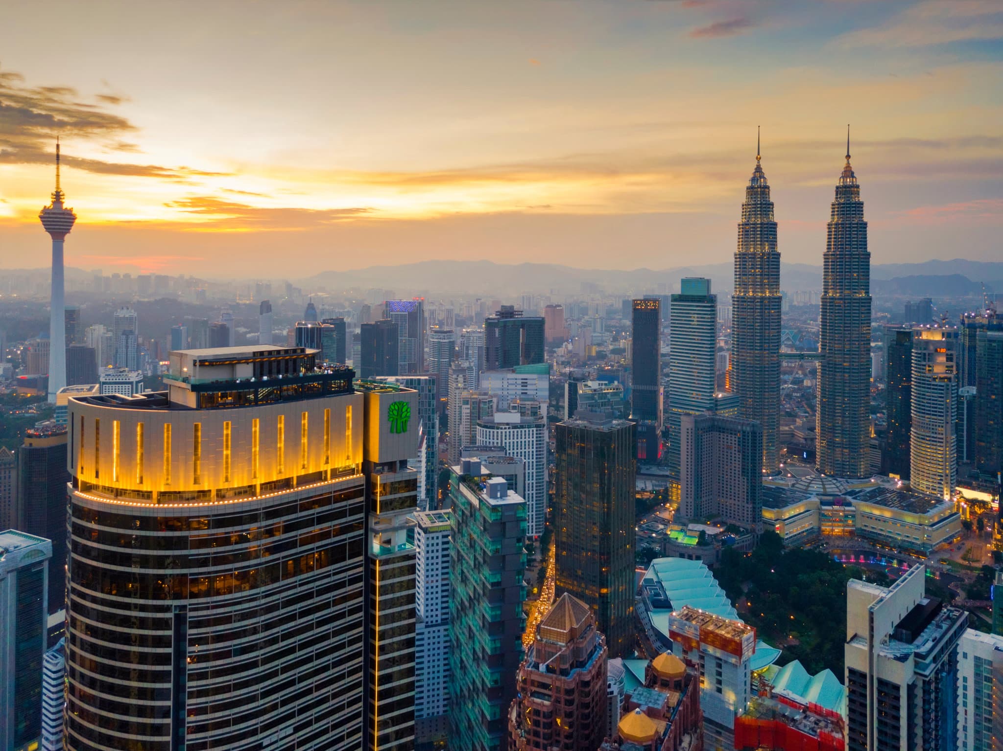 A woman in a white swimsuit looking out at the Petronas Twin Towers from the edge of the Banyan Tree Kuala Lumpur infinity pool at sunset.