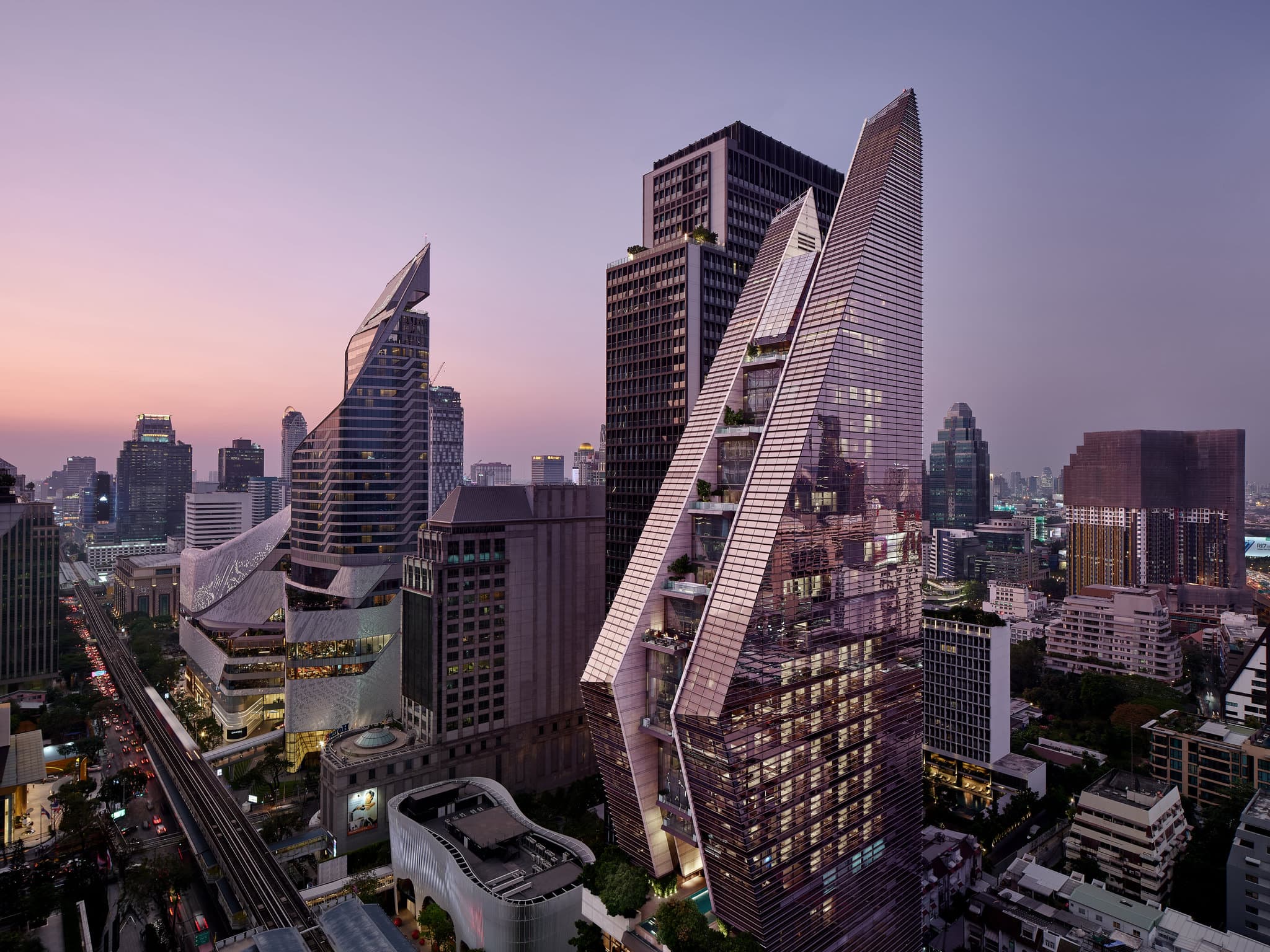 The dramatic geometric facade of Rosewood Bangkok illuminated at twilight, resembling the Thai 'wai' hand gesture.