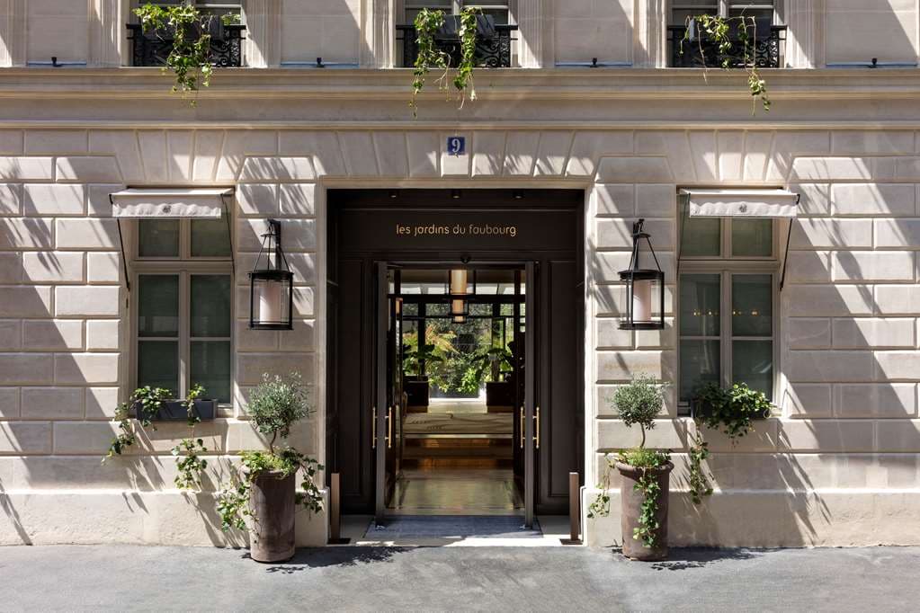 Diners enjoying the lush, open-air courtyard garden of Les Jardins du Faubourg in Paris, surrounded by ivy-covered walls.