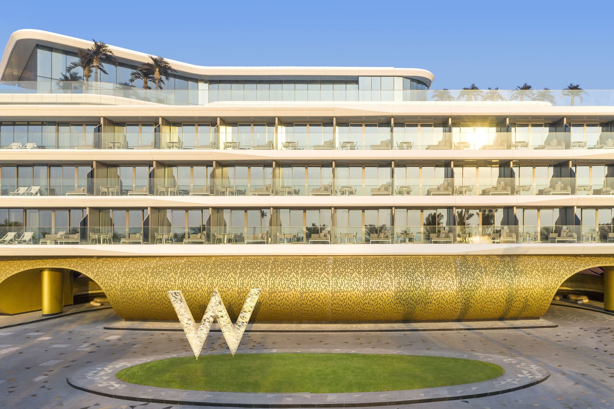 The curving, illuminated exterior of W Dubai - The Palm at twilight, reflecting over the segmented WET Deck pools.