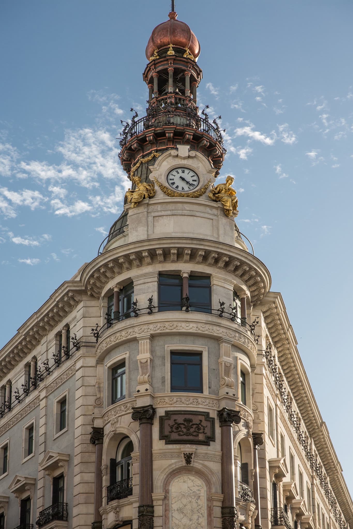 High-angle shot of the Four Seasons Madrid's spiral Oval Staircase with gold railings and marble floors.