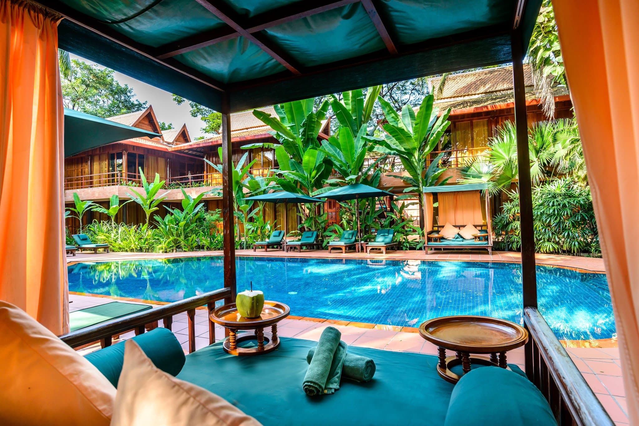 Wooden walkways of Angkor Village Hotel winding through lush tropical gardens and lotus ponds at twilight.