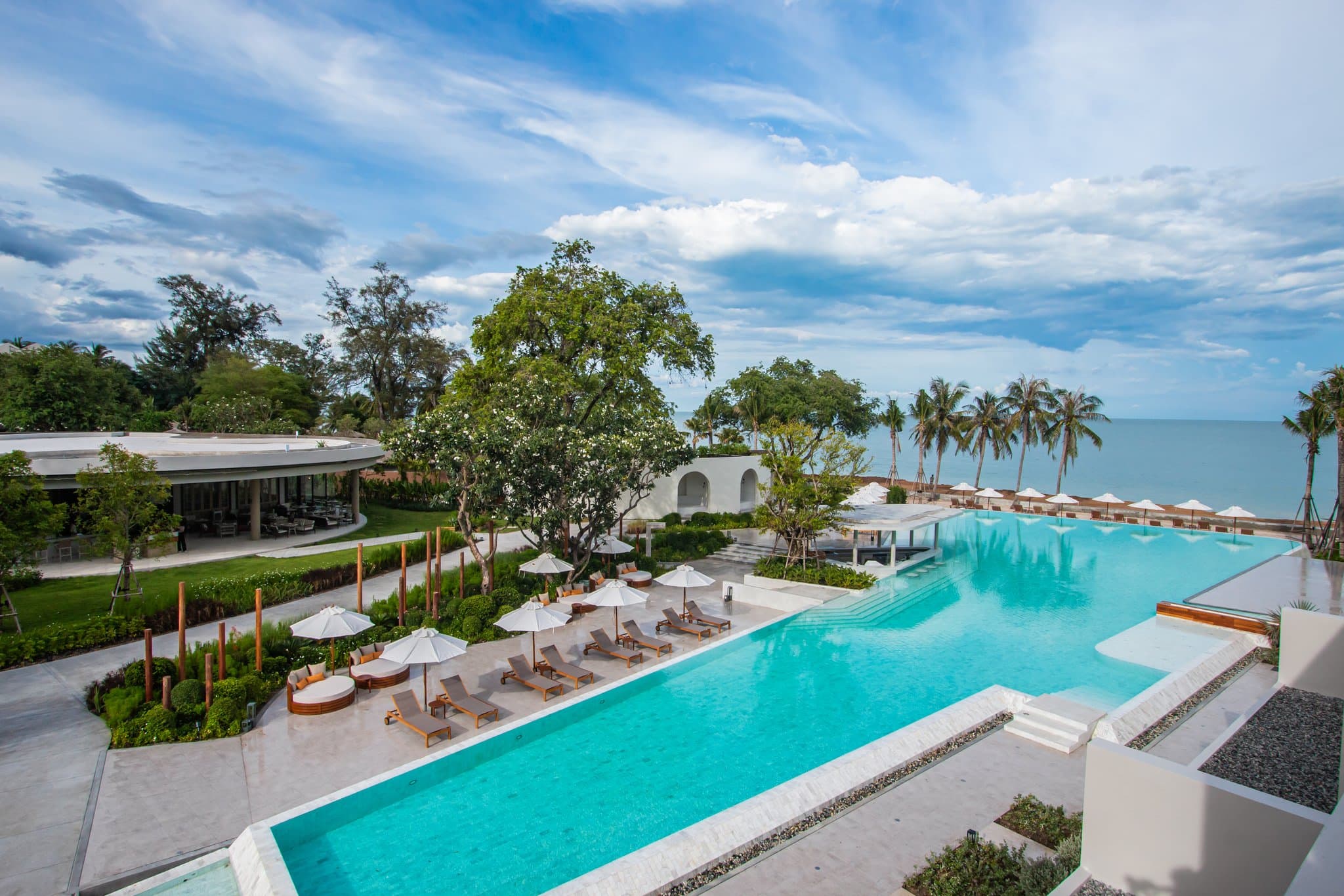 Aerial view of VALA Hua Hin's Olympic-length white marble infinity pool bordering the beach at sunrise.