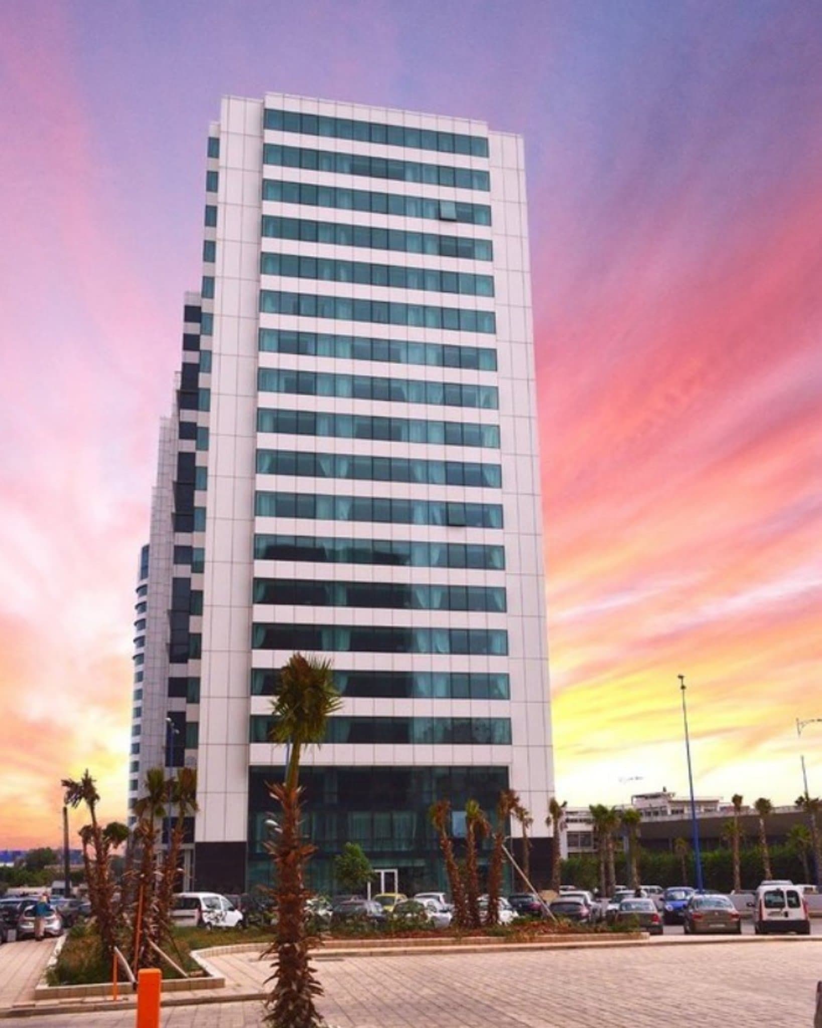 Low angle view of the Hotel Mogador Marina's reflective glass facade towering against a blue sky.